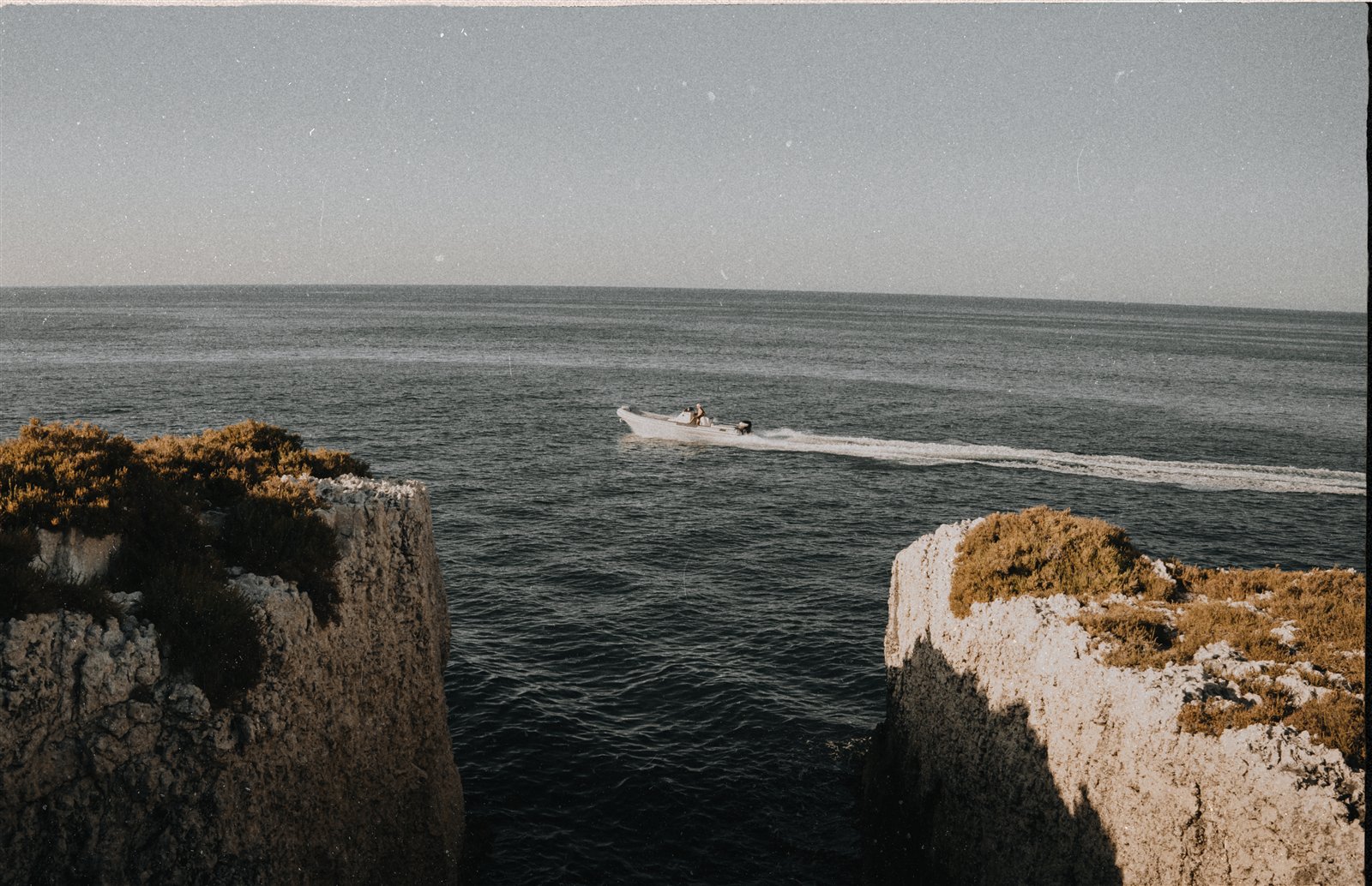 A small motorboat passing between two rocky sea cliffs