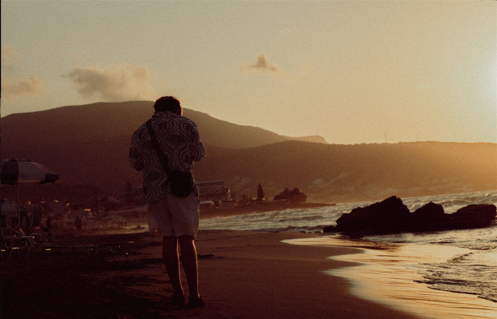 A person standing on a beach at sunset with mountains across the bay